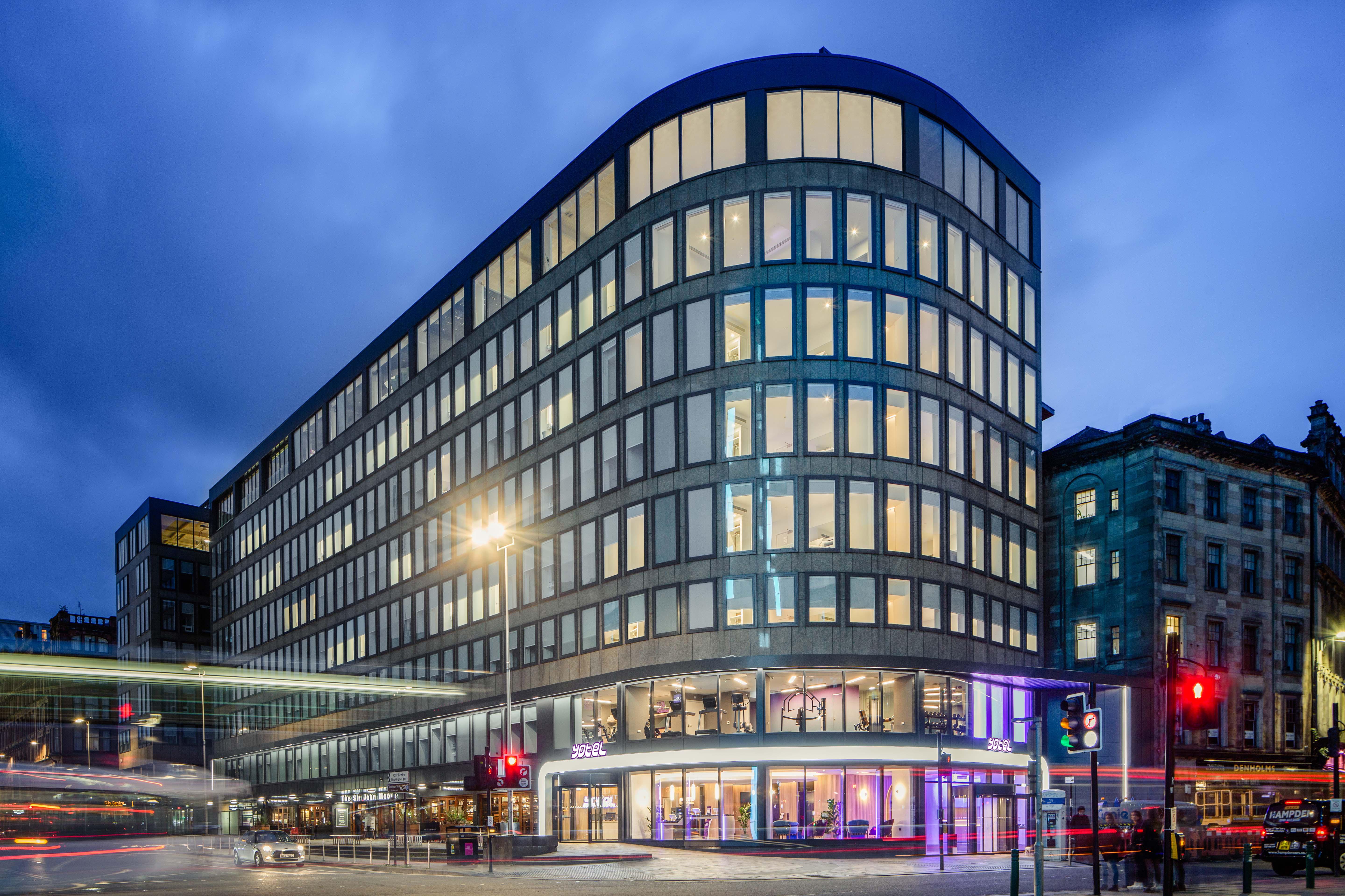 Yotel Glasgow Dış mekan fotoğraf The photo shows a modern office building with a distinctive curved shape and a facade made of large glass windows. It is illuminated against a twilight sky, giving it a contemporary appearance. The ground floor features large glass entrance areas, li